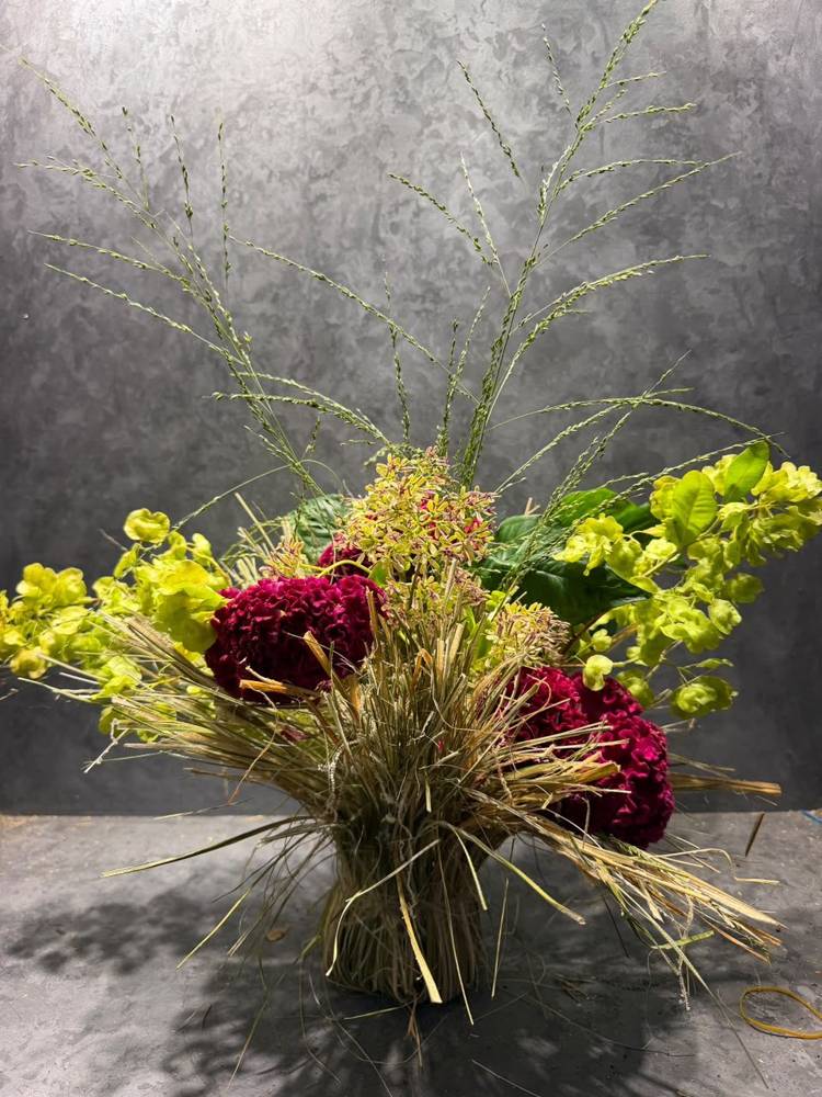 Magenta celosia and lime foliage bursting from a sheaf of dry grass