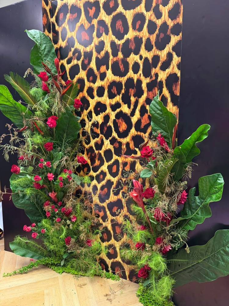 A tall installation of red roses, ginger and oversized leaves framing a leopard-print backdrop