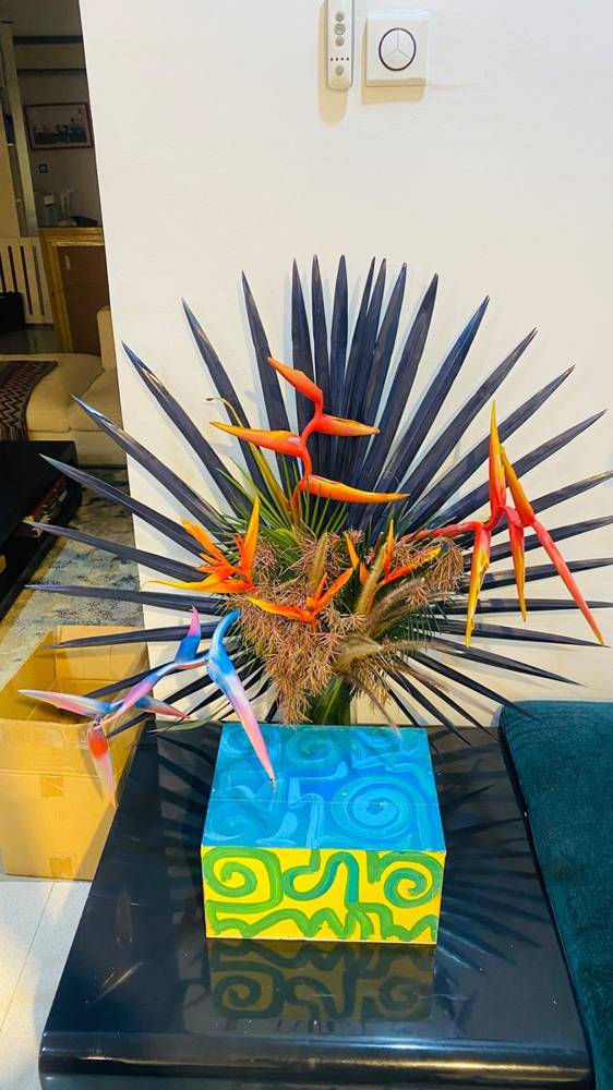 Heliconia, blue bird of paradise and a painted palm fan on a living-room console