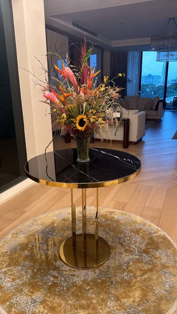 A tall arrangement of heliconia, ginger and sunflowers on a marble entrance table