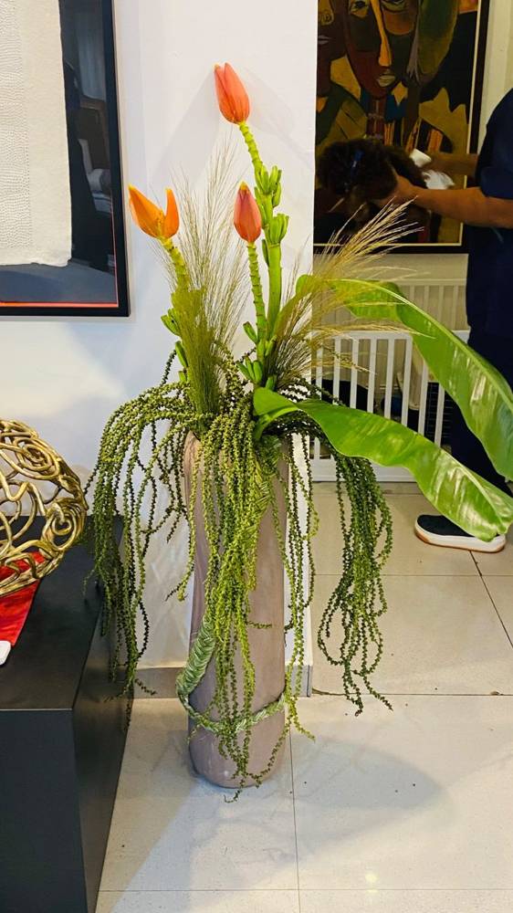 Orange banana flowers and trailing green in a tall floor vase