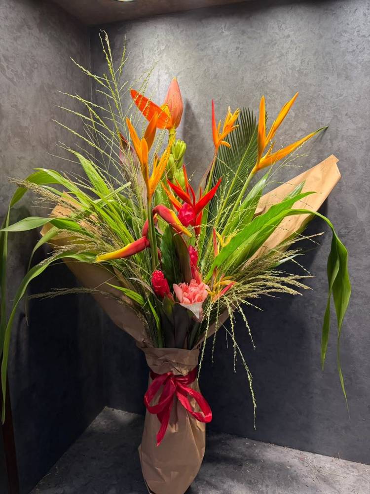 A hand-tied bouquet of heliconia, ginger and grasses wrapped in kraft paper with a red ribbon