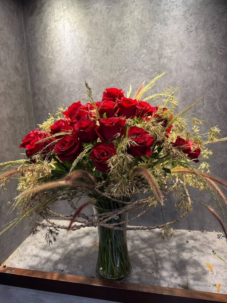 Red roses with grasses and curled leaf in a glass vase