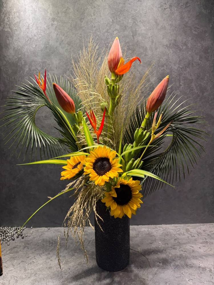 Heliconia and sunflowers rising from a sheaf tied with braided grass